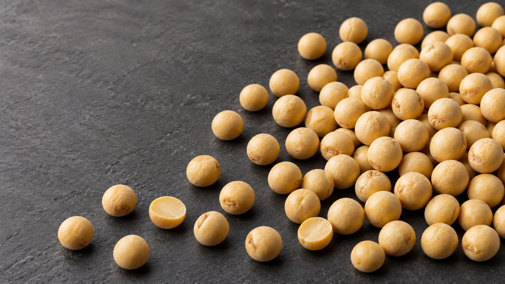Round whole yellow field peas and thick split pea halves on a dark surface.